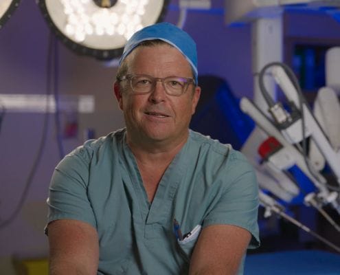 Dr. Jeff McCracken, Chief Urologist & Head of Robotics at Royal Jubilee & Victoria General Hospitals sitting in front of the Da Vinci Surgical Robot